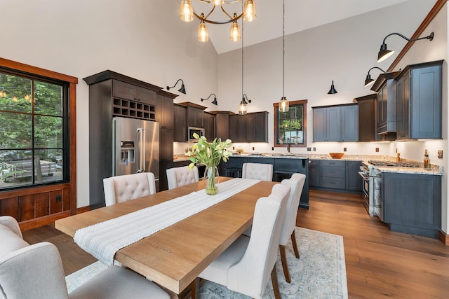 dining space with high vaulted ceiling, sink, an inviting chandelier, and light hardwood / wood-style flooring