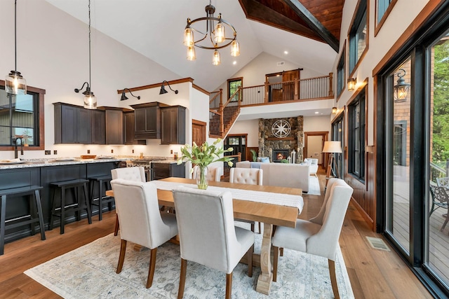 dining room featuring a notable chandelier, a stone fireplace, high vaulted ceiling, and light wood-type flooring