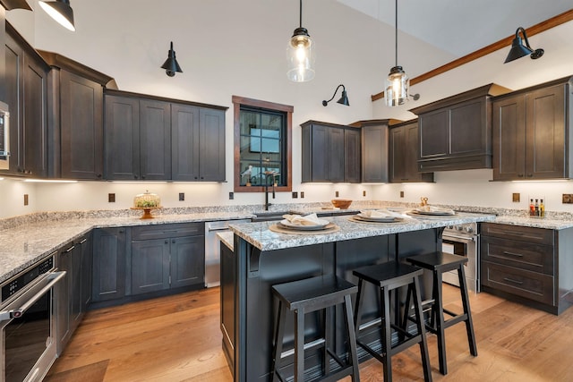 kitchen featuring a kitchen island, appliances with stainless steel finishes, pendant lighting, light stone counters, and dark brown cabinets