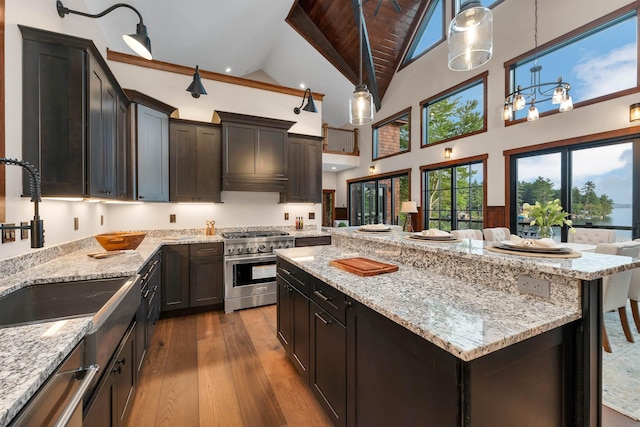 kitchen with hardwood / wood-style floors, a kitchen breakfast bar, hanging light fixtures, stainless steel appliances, and light stone countertops