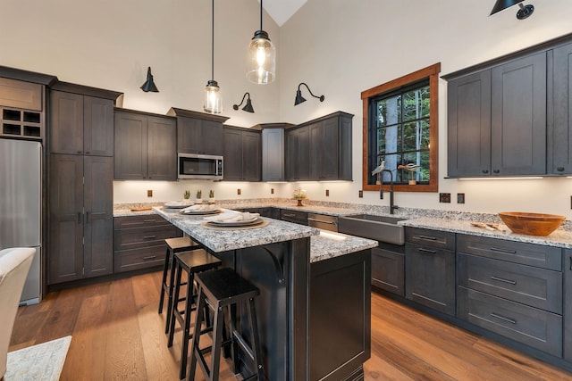 kitchen with sink, decorative light fixtures, a center island, appliances with stainless steel finishes, and light stone countertops