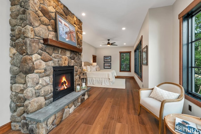 living room featuring hardwood / wood-style flooring, ceiling fan, and a stone fireplace