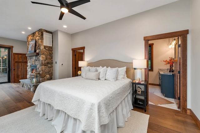 bedroom featuring ceiling fan, wood-type flooring, and a stone fireplace