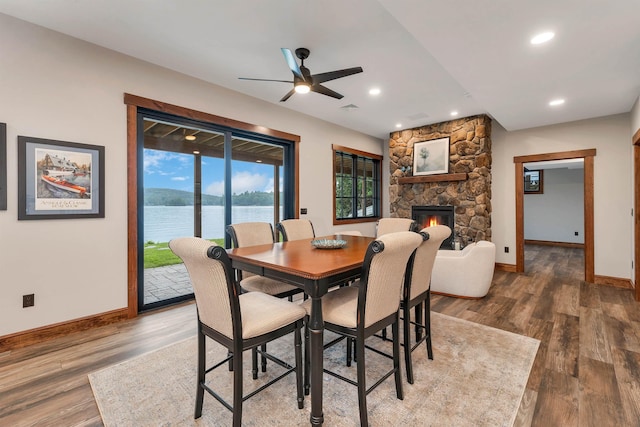 dining area with a water view, hardwood / wood-style floors, a stone fireplace, and ceiling fan