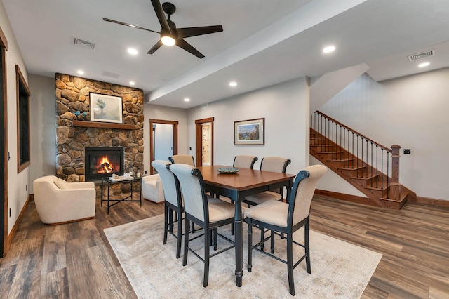 dining area featuring a stone fireplace, wood-type flooring, and ceiling fan