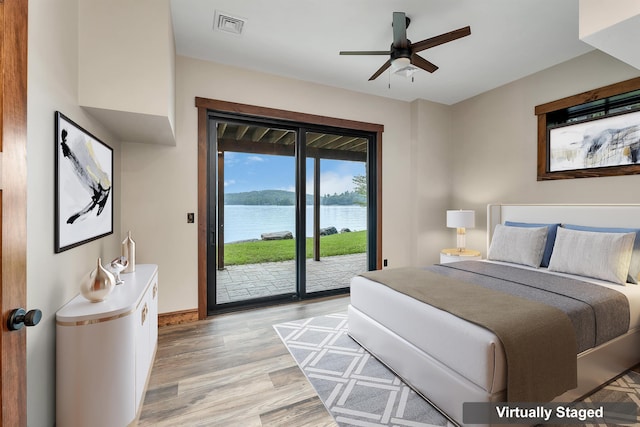 bedroom featuring access to exterior, light hardwood / wood-style floors, and a water view