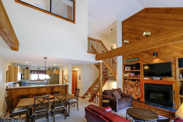 living room with stairs, high vaulted ceiling, carpet flooring, and a tiled fireplace