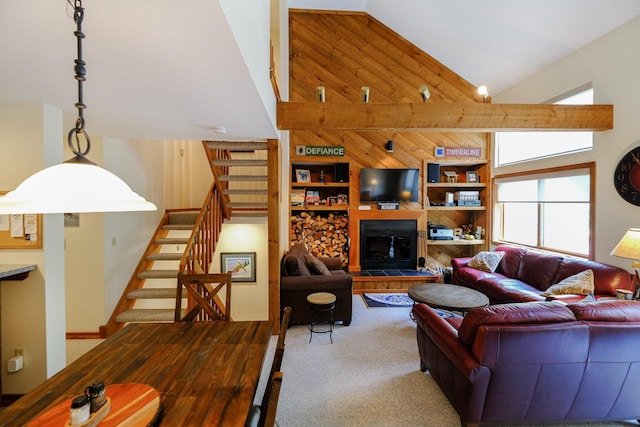 living room with wood walls, stairs, high vaulted ceiling, and a fireplace with raised hearth