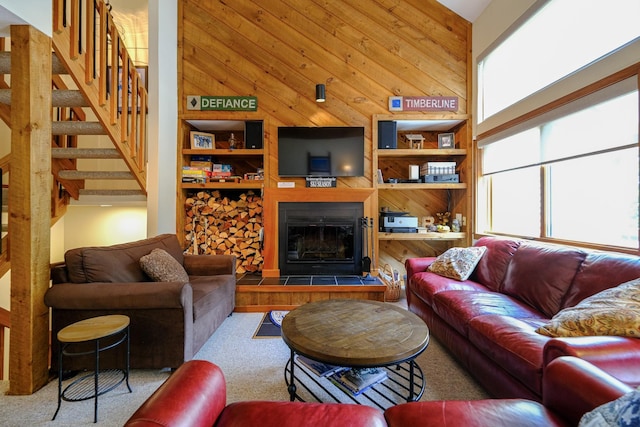 living room featuring built in shelves, stairway, carpet flooring, wooden walls, and a tile fireplace