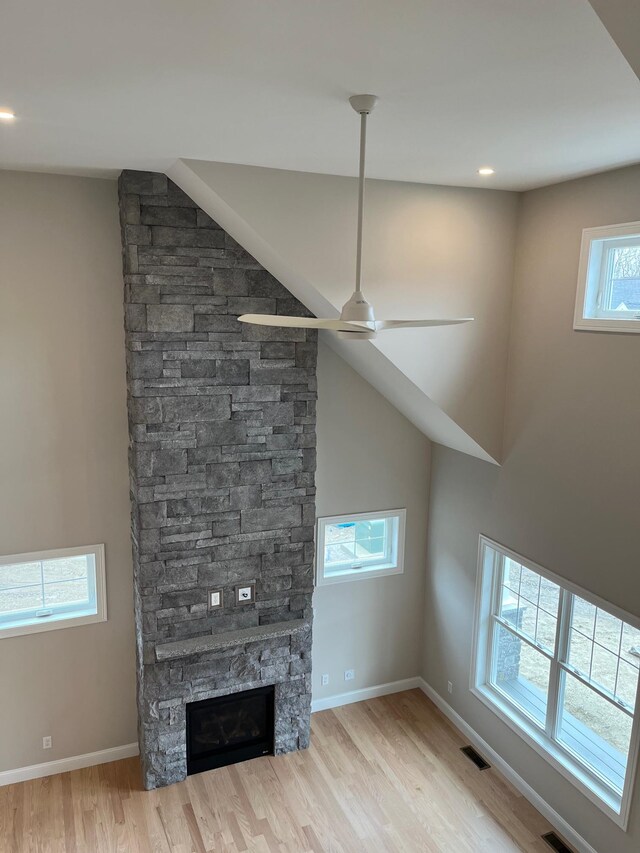 unfurnished living room with a stone fireplace, light wood-type flooring, and ceiling fan