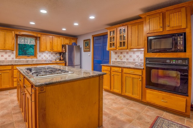 kitchen featuring light stone counters, decorative backsplash, a kitchen island, and black appliances