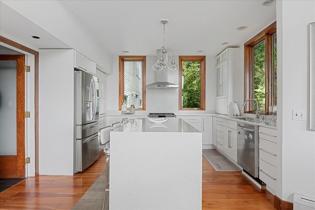 kitchen featuring appliances with stainless steel finishes, light wood-type flooring, a kitchen island, white cabinets, and hanging light fixtures