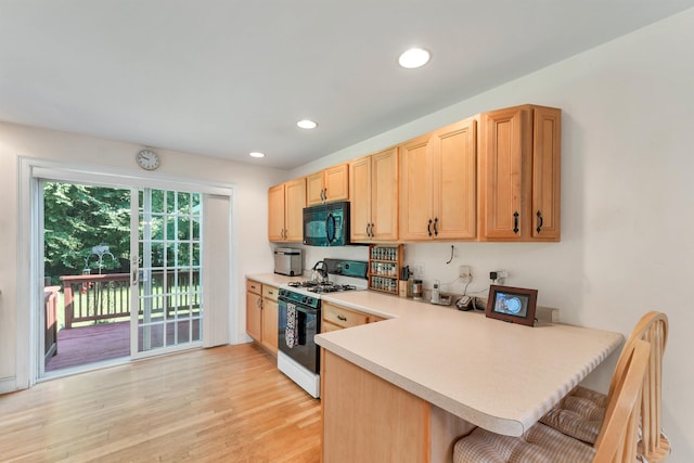 kitchen featuring a breakfast bar area, a peninsula, gas range oven, light countertops, and black microwave