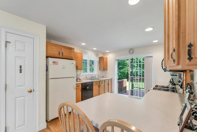 kitchen featuring black dishwasher, light wood-style flooring, freestanding refrigerator, a peninsula, and a sink