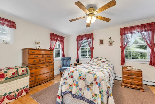 bedroom featuring multiple windows, baseboard heating, wood finished floors, and a ceiling fan