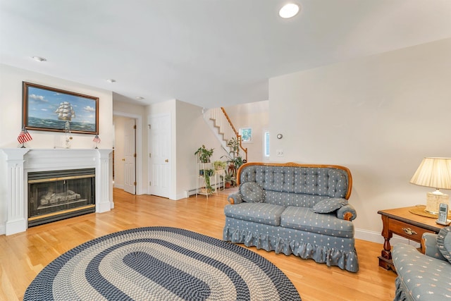 living room with a glass covered fireplace, stairway, baseboards, and wood finished floors