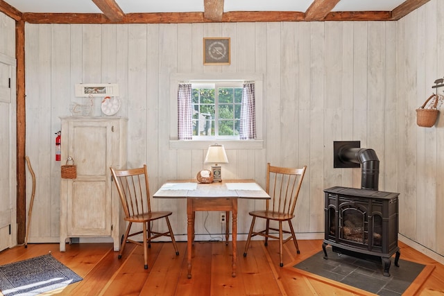 living area with beamed ceiling, wood walls, light hardwood / wood-style flooring, and a wood stove