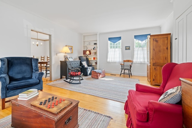 living room featuring an inviting chandelier, built in shelves, light hardwood / wood-style flooring, and ornamental molding