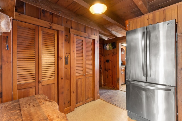 kitchen featuring beam ceiling, freestanding refrigerator, light carpet, wooden walls, and wooden ceiling