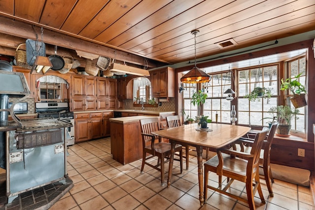 kitchen featuring light countertops, backsplash, gas stove, light tile patterned flooring, and wooden ceiling