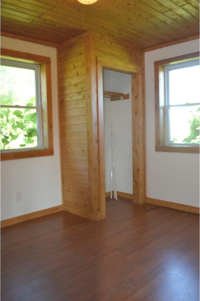 unfurnished bedroom featuring wooden ceiling, dark wood-type flooring, and wooden walls