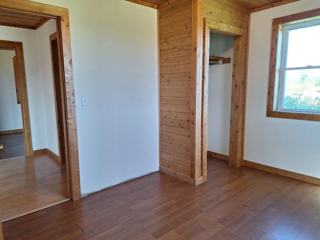 unfurnished bedroom with hardwood / wood-style floors, a closet, and wood walls