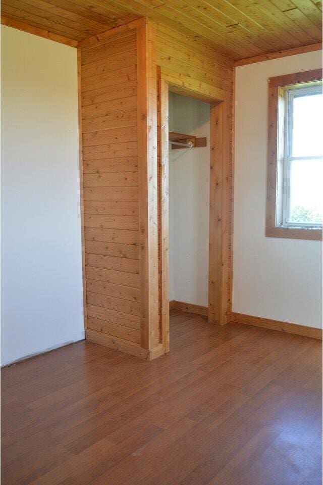 unfurnished bedroom featuring hardwood / wood-style flooring, wooden ceiling, a closet, and wood walls