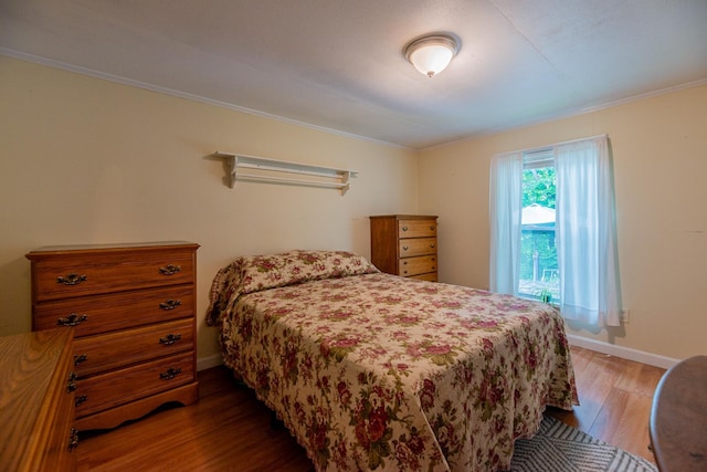 bedroom featuring baseboards, wood finished floors, and crown molding