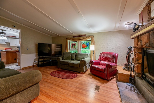 living area featuring visible vents, lofted ceiling, light wood-style flooring, a stone fireplace, and a textured wall