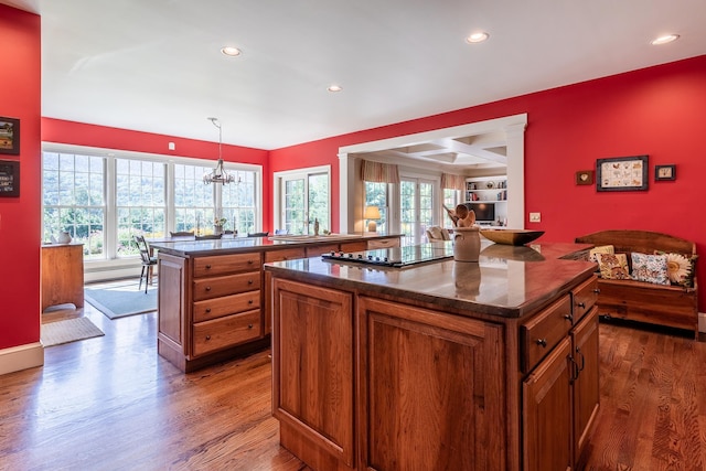 kitchen featuring black electric cooktop, a peninsula, wood finished floors, brown cabinets, and decorative light fixtures