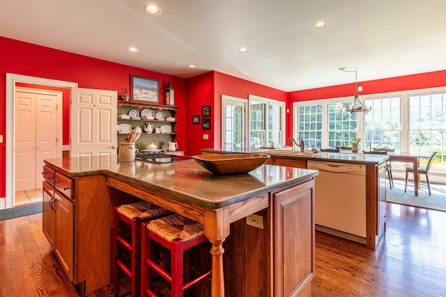 kitchen featuring a breakfast bar area, white dishwasher, a kitchen island, hanging light fixtures, and open shelves