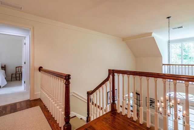 stairs with an inviting chandelier, crown molding, visible vents, and wood finished floors