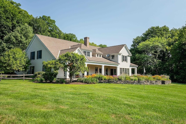 back of house with covered porch, a lawn, and a chimney