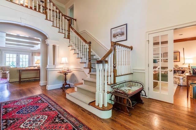 stairs with a high ceiling, wood finished floors, ornamental molding, french doors, and decorative columns