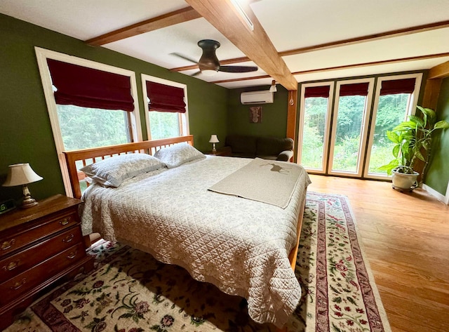 bedroom featuring beamed ceiling, a wall mounted air conditioner, ceiling fan, and light wood-type flooring