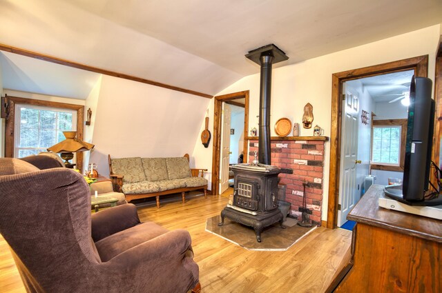 living room featuring ceiling fan, light wood-type flooring, lofted ceiling, and a wood stove