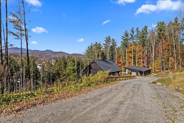 view of road featuring a mountain view, a wooded view, and dirt driveway