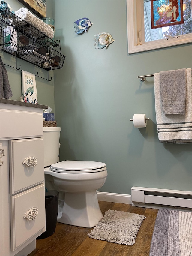 bathroom with toilet, a baseboard heating unit, baseboards, and wood finished floors