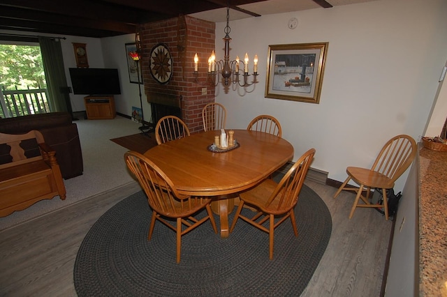 dining room featuring a fireplace, wood-type flooring, brick wall, and an inviting chandelier