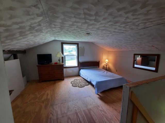 bedroom featuring vaulted ceiling, a textured ceiling, and wood finished floors