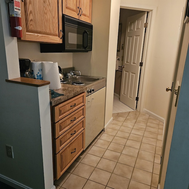 kitchen featuring baseboards, a sink, light tile patterned floors, black microwave, and dark stone counters