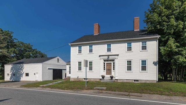 colonial house featuring entry steps, a front lawn, a chimney, and an outbuilding