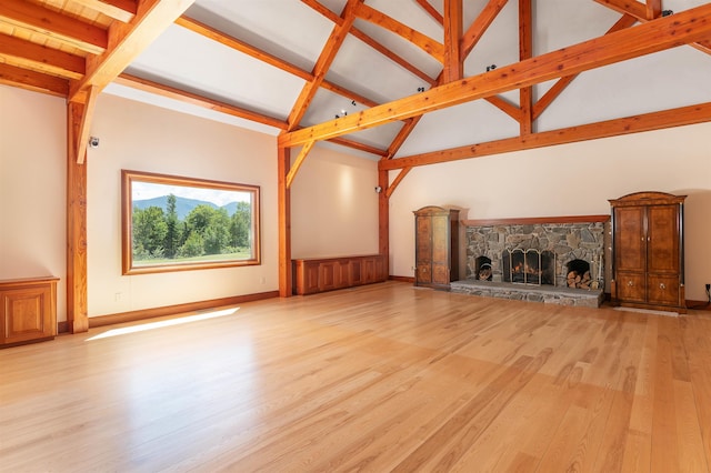 unfurnished living room featuring a stone fireplace, high vaulted ceiling, beam ceiling, and light hardwood / wood-style flooring