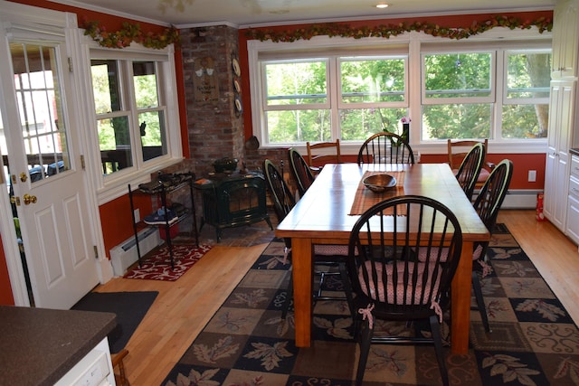 dining space featuring a baseboard radiator, brick wall, a wood stove, and hardwood / wood-style floors