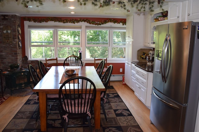 dining room featuring brick wall, a wealth of natural light, baseboard heating, and light hardwood / wood-style flooring