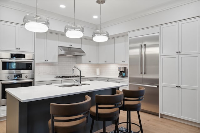 kitchen with appliances with stainless steel finishes, light hardwood / wood-style floors, a center island with sink, decorative light fixtures, and backsplash