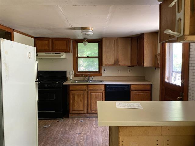 kitchen featuring light countertops, brown cabinetry, a sink, under cabinet range hood, and black appliances