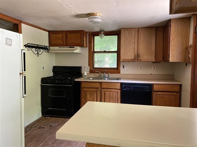 kitchen featuring under cabinet range hood, a sink, light countertops, brown cabinets, and black appliances