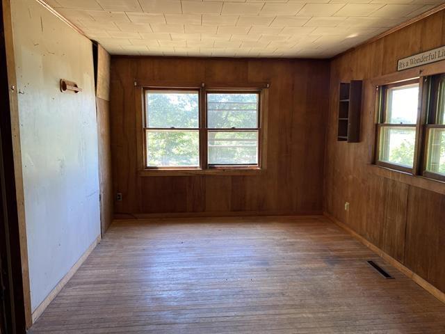 spare room with wood walls, wood-type flooring, visible vents, and baseboards