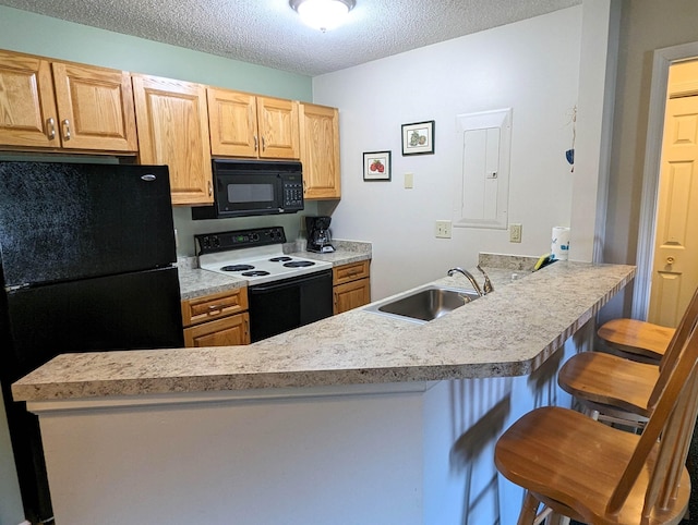 kitchen featuring a peninsula, a sink, light countertops, black appliances, and a kitchen bar